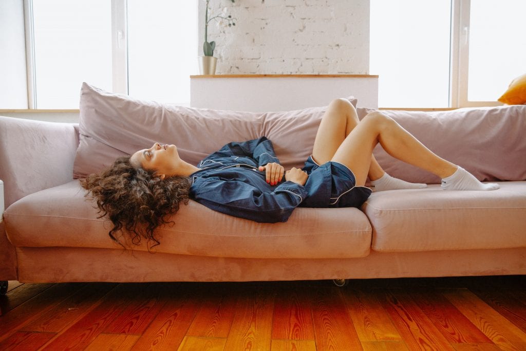 woman lays on couch holding stomach in pain